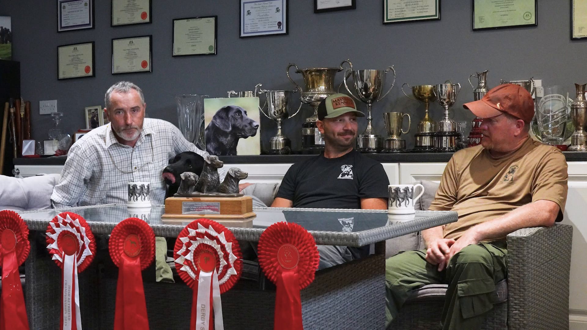 Three GRS trainers talking in the trophy room, surrounded by cups and rosettes